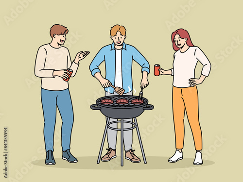 BBQ party with cheerful friends drinking beer and grilling meat on grill in park or in backyard of house. Happy people celebrating start of summer vacation and cooking beef meat on BBQ coals