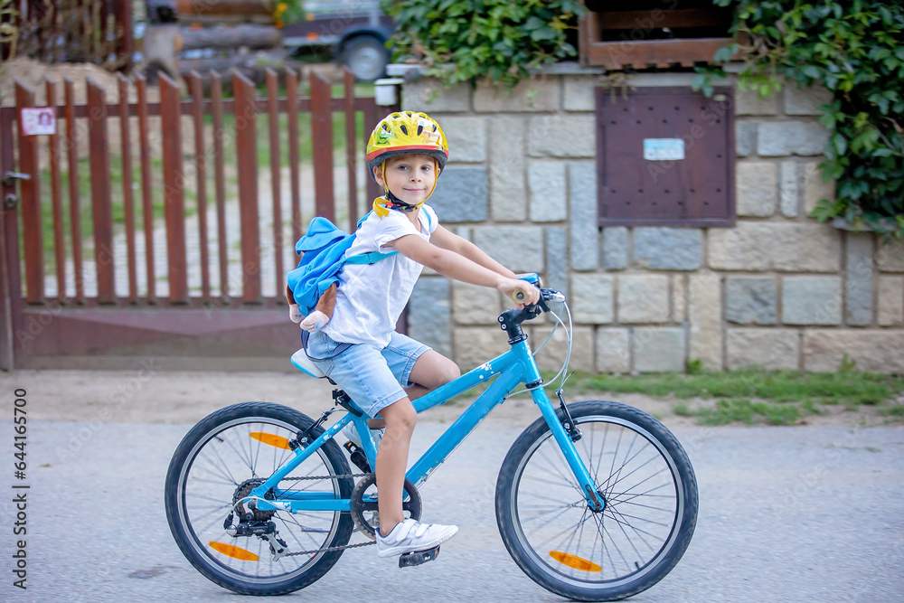 Fototapeta premium Cute child, boy with helmet and backpack, riding bike at the evening in rural nature