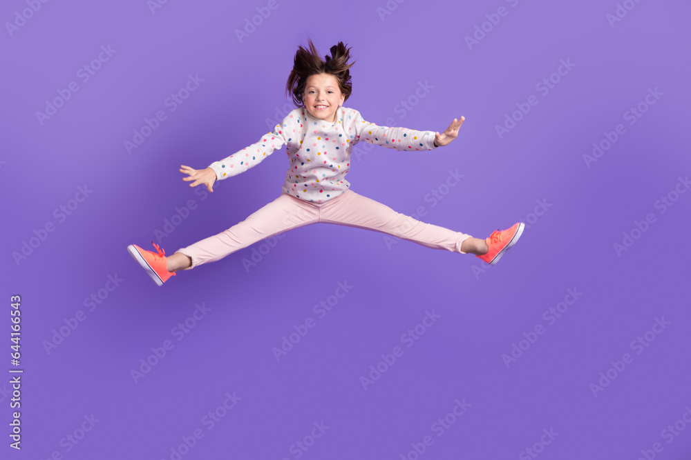 Full length photo of excited funky little girl dressed dotted pullover jumping high isolated purple color background Full length photo of excited funky little girl dressed dotted pullover jumping high isolated purple color background