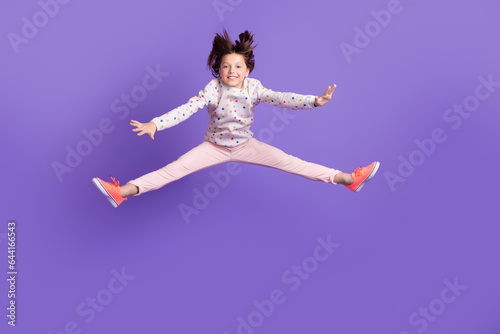 Full length photo of excited funky little girl dressed dotted pullover jumping high isolated purple color background