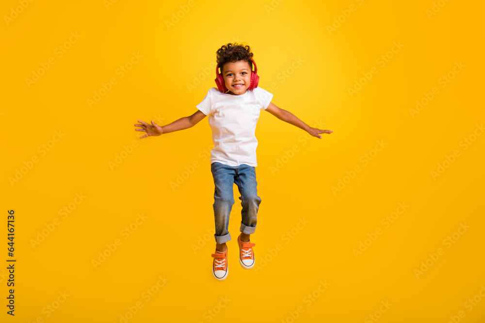 Full length photo of sweet positive little boy dressed white t-shirt jumping high enjoying songs earphones isolated yellow color background