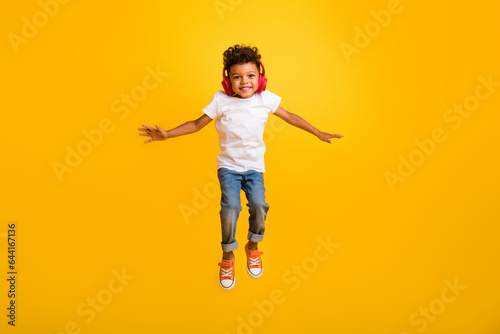 Full length photo of sweet positive little boy dressed white t-shirt jumping high enjoying songs earphones isolated yellow color background