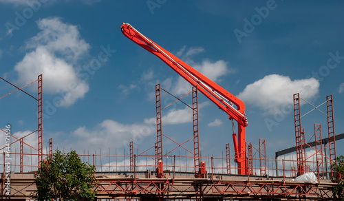 A bright orange Cement Crane Pump at a Construction Site against a blue sky with clouds