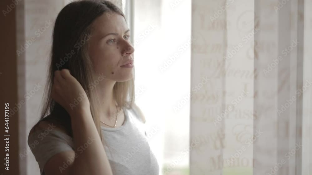 The girl is standing at the window and looking out The girl is standing at the window and looking out