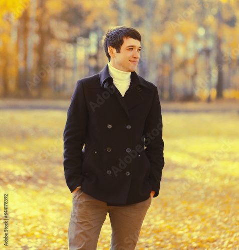 Portrait of elegant caucasian young man in black coat outdoors in autumn park with yellow leaves