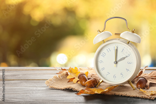 Alarm clock, acorns and autumn leaves on table outdoors. Daylight saving time end