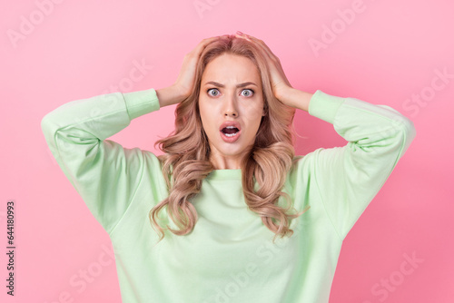 Portrait of funny young woman open mouth speechless crazy unhappy wearing green pullover staring isolated on pink color background