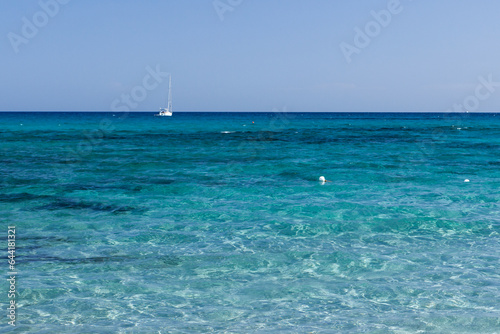 Clear blue water of Mediterranean sea and sailboat anchored near the coast at Sardinia, Italy on sunny day.