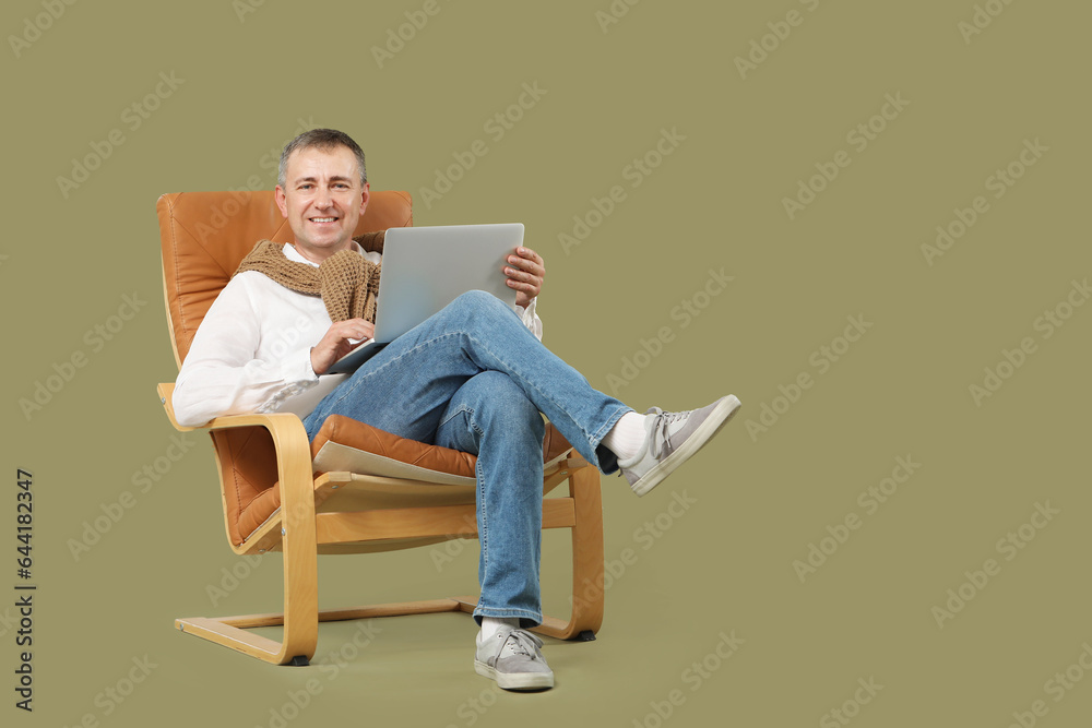 Mature man with laptop messaging in armchair on green background Mature man with laptop messaging in armchair on green background