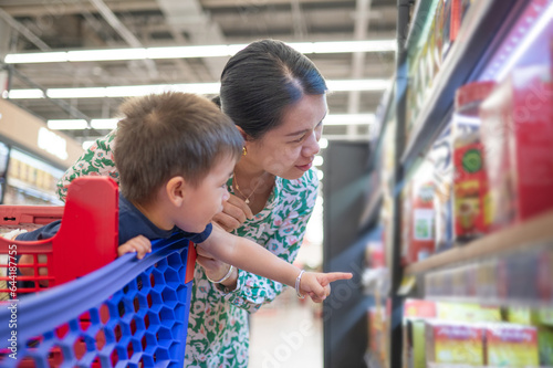 Asian mom and her little multiracial boy in shopping trolley are shopping for groceries in the supermarket