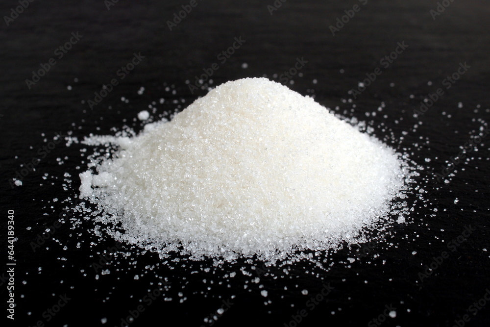 A pile of crumbly sugar in a heap lie on a black background.