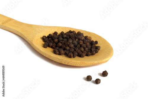 On a white background lies a wooden spoon with seasoning black peppercorns.