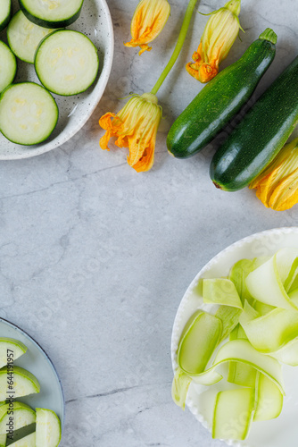 Pieces of sliced zucchini squash on white plate on marbel background. Flat lay, top view. Vegetarism concept. vertical. photo