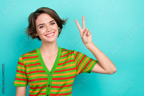 Photo of cute positive woman dressed striped t-shirt showing v-sign empty space isolated turquoise color background