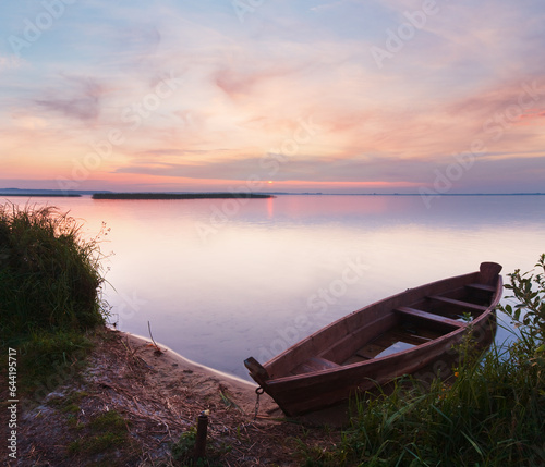 Sunset and old wooden flooding boat near the summer lake shore  Svityaz  Ukraine 