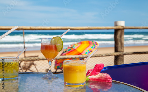 Drinks tropicais em mesa de praia no nordeste do Brasil. No fundo ondas do mar e um guarda sol colorido photo