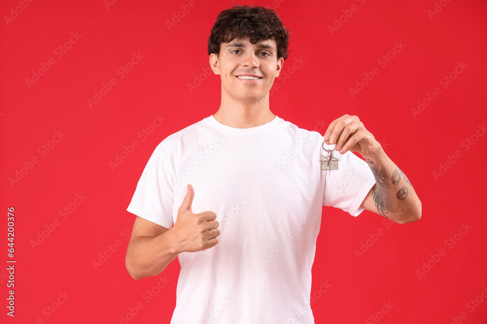 Young man with keys from house showing thumb-up on red background