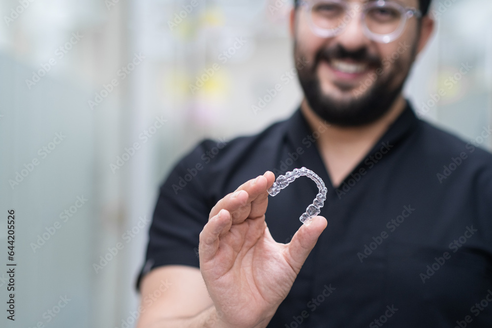 Positive dentist demonstrating clear aligners used for effective teeth straightening in contemporary stomatology center doctor holding device in clinic closeup