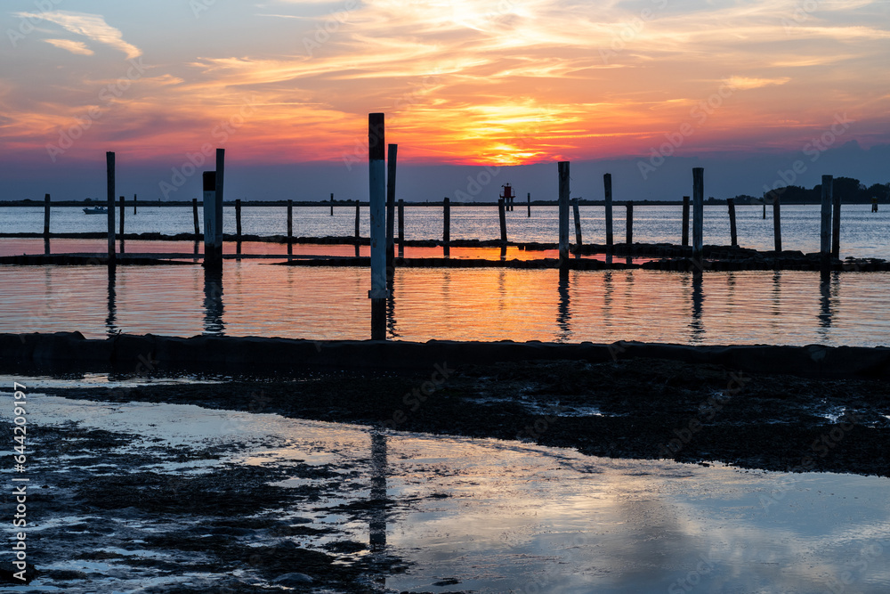 Sunset on the Grado Lagoon during a summer day. The sun is about to disappear over the horizon. Orange color and warm tones. A beautiful reflection on the sea. Taken near the Port.