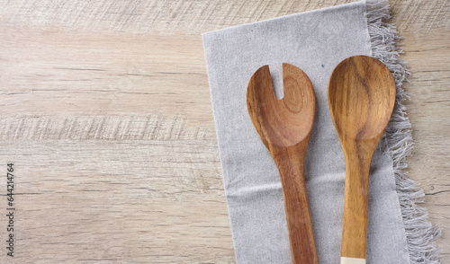 Two wooden spoons on a gray textile kitchen towel on a wooden background, top view