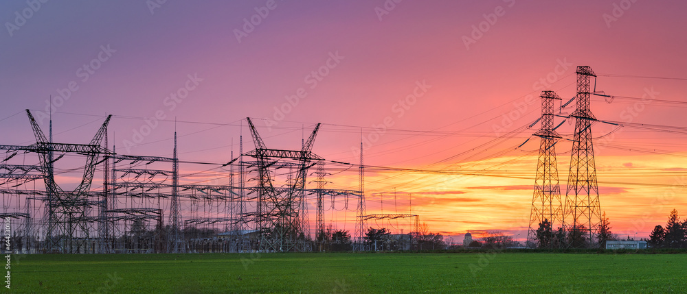 High voltage lines with high masts in the field, colorful sky in orange pink shades after sunset.