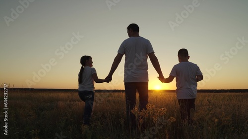 Family, dad, daughter, son go hand in hand outdoors in summer, Silhouette. Parental care for children. Happy family, group of people, nature. Dad with children, boy, girl walks through field at sunset