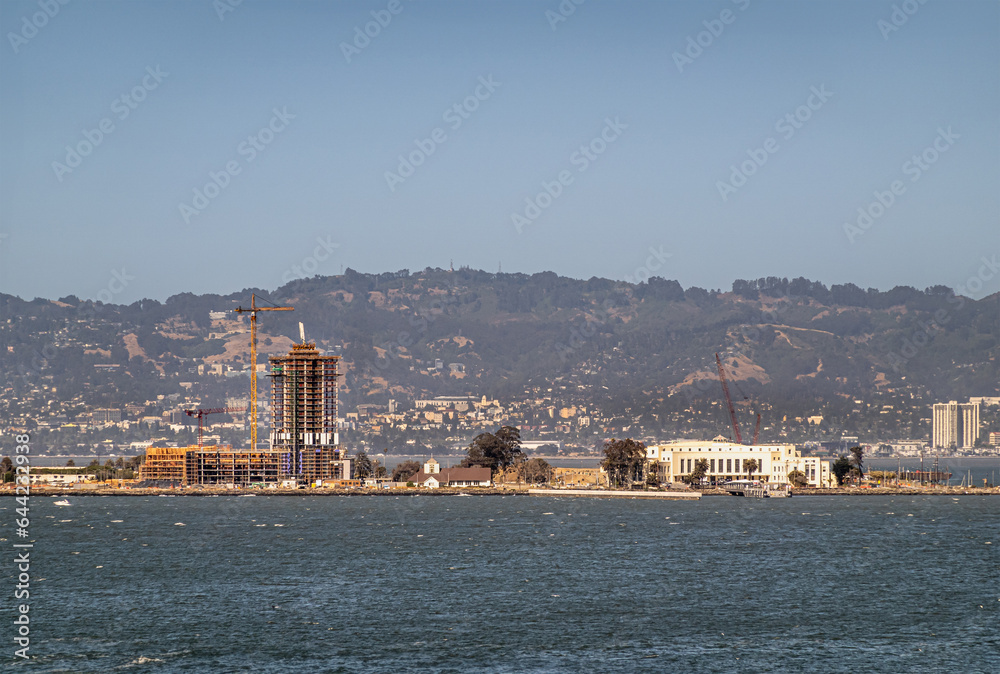 San Francisco, CA, USA - July 13, 2023: Crane and building skeleton on construction site, Treasure Island, Bay water and buildings and mountains of the east bay