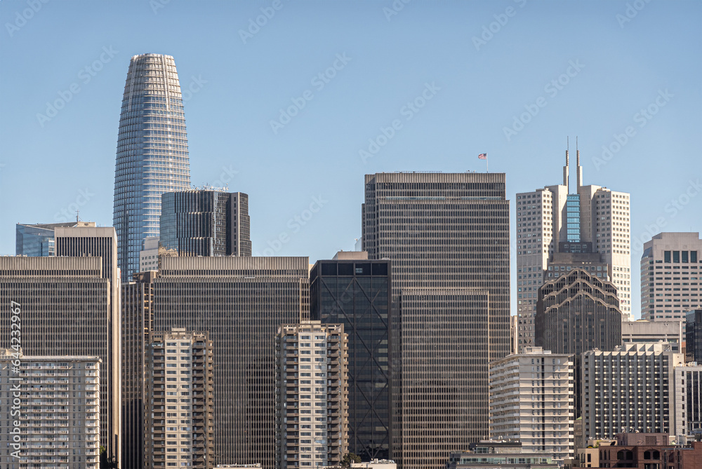 San Francisco, CA, USA - July 13, 2023: Urban jungle of tall skyscrapers with Salesforce building peeking over the rest and California Center with its 2 sharp spires to the right, Light blue sky