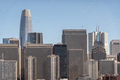 San Francisco, CA, USA - July 13, 2023: Urban jungle of tall skyscrapers with Salesforce building peeking over the rest and California Center with its 2 sharp spires to the right, Light blue sky