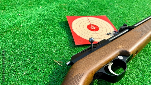 Photography air rifle for training with its target and its pellets on the grass