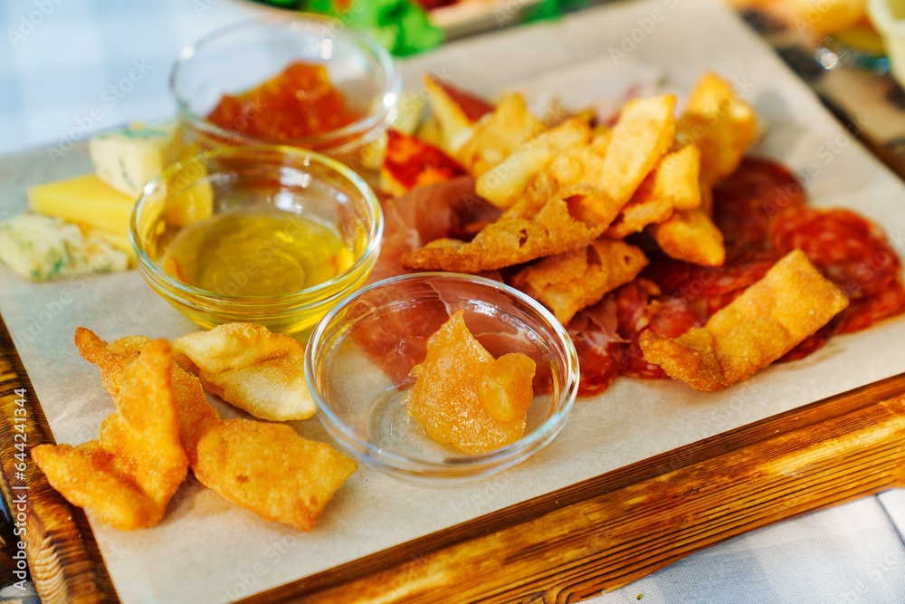 A wooden tray with chips, honey, sauce, cheese and meat appetizers A wooden tray with chips, honey, sauce, cheese and meat appetizers