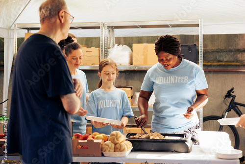 Group of female volunteers at community center distributing free food to people in need. African American woman preparing a meal to give to hungry homeless man at food drive.