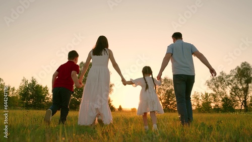 Happy family holding hands running towards sun and having fun in city park at sunset. Slow motion. Family, mom, dad daughter run together, happy childhood, freedom people, future, family game concept