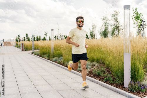 A male runner in running shoes, running a distance cardio workout. A full-length athlete in sportswear is engaged in fitness in the city. Uses a fitness watch and an app.