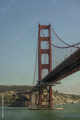 Fototapeta Naklejka Na Ścianę i Meble -  San Francisco, CA, USA - July 13, 2023: Portrait, south alnding and tower of Golden Gate bridge under light blue evening sky. Presidio hills and ocean shoreline