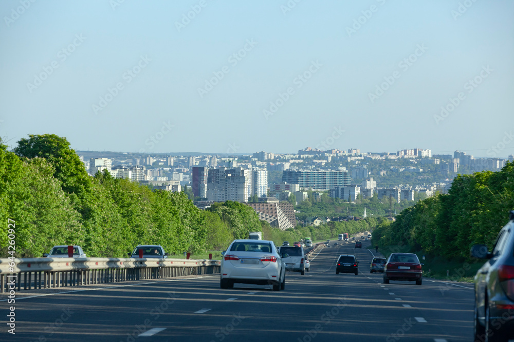 Vehicles and traffic. Multi-lane highway against the backdrop of a green city.