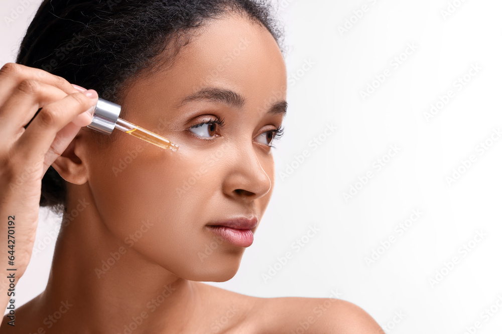 Beautiful woman applying serum onto her face on white background, closeup. Space for text Beautiful woman applying serum onto her face on white background, closeup. Space for text