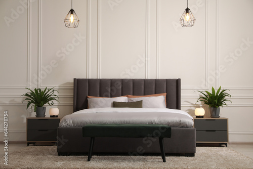 Stylish bedroom interior with large comfortable bed and ottoman