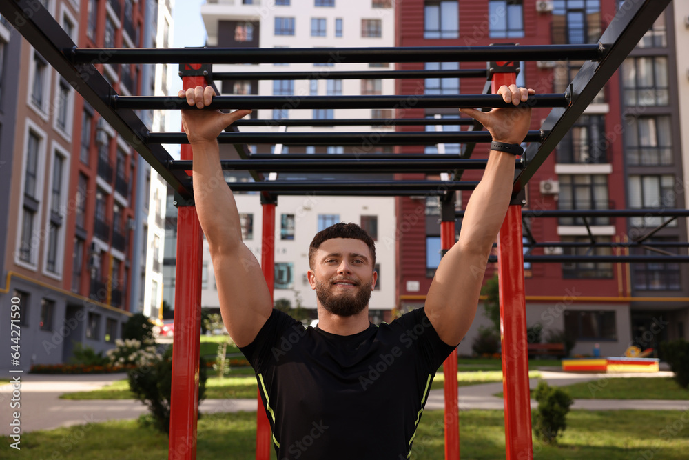 Naklejka premium Smiling man training on monkey bars at outdoor gym