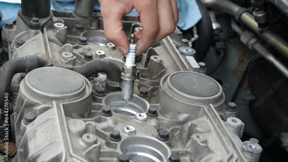 Fototapeta premium Close up of hand inserting new spark plug into old engine 