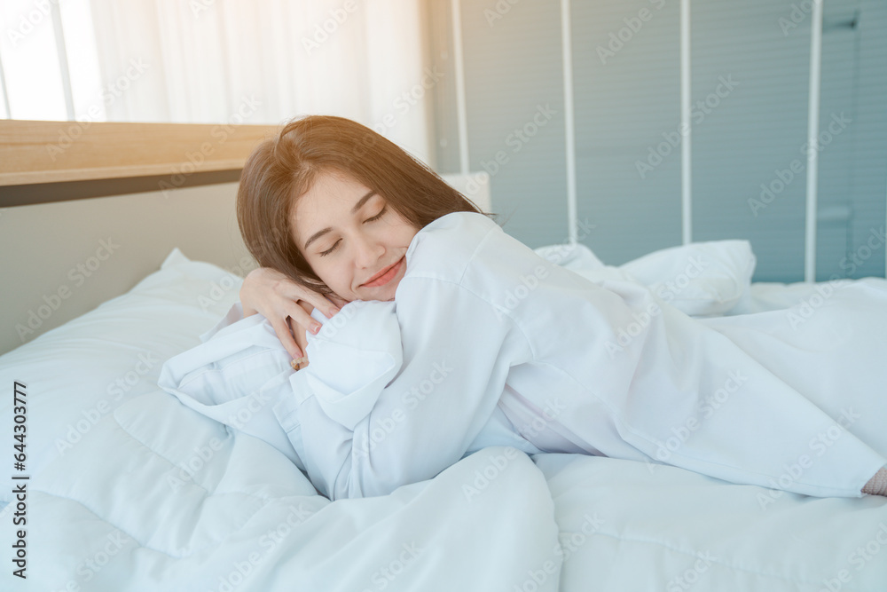 Photo of young happy woman in pajama stretching her arms and smiling while sitting on bed after sleep Photo of young happy woman in pajama stretching her arms and smiling while sitting on bed after sleep