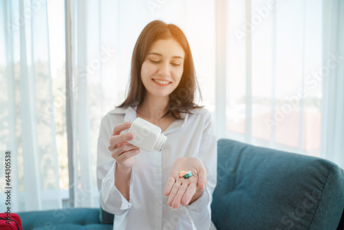 Portrait of relaxed asian young woman taking medicine and measuring temperature with thermometer, Infected patient at home medical self treatment, self recover health care concept. 