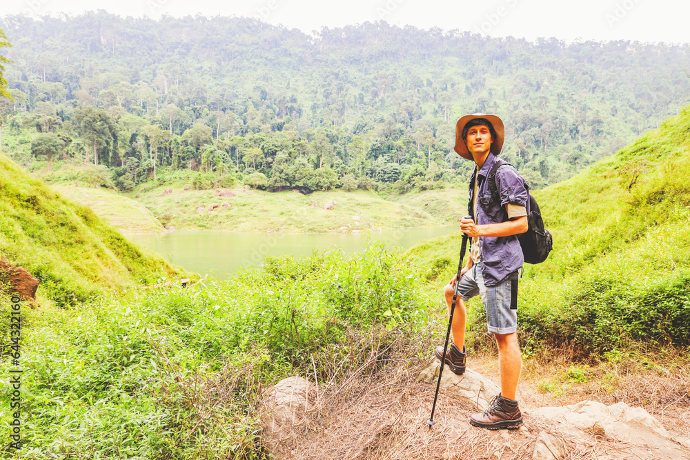 Young caucasian male adventurer backpacking hiking trip through Thailand's tropical forests standing looking at the sky mountains rivers and lush forests nature's beauty and fresh air.