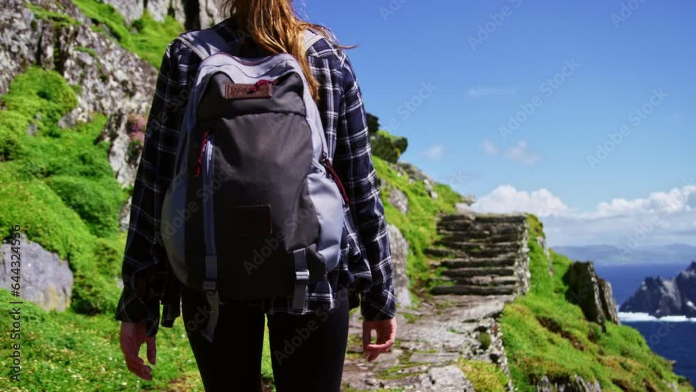 Woman with backpack hiking cliff face in Ireland