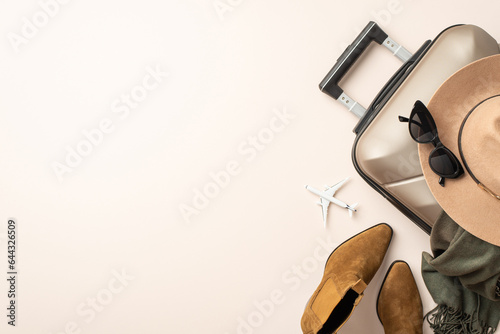 Sophisticated flying concept. Miniature plane model surrounded by classy items - felt hat, cat-eye shades, scarf, ankle boots, suitcase on neutral pastel background with empty space for advert