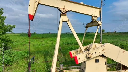 Oil well pumping crude oil out of field. Aerial close up rising shot of well in action.
