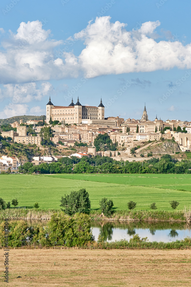 Image of the old town of Toledo with detail of the eastern area with the fortress dominating the urban landscape with green fields and the Tagus River in the foreground