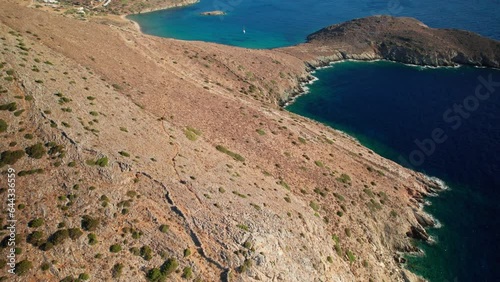 Aerial bird's eye view tilt up along dry coastline of syros greece, reveals sailboat and peninsula photo