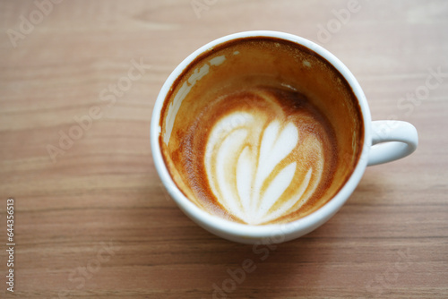Half cup of hot latte art in heart shaped after drink on wooden table background. Copy space.
