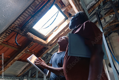 Architect and builder holding solar panel and looking through ceiling window in attic photo